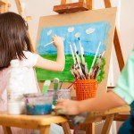 Rear view of some kids working on a painting and drawing some clouds for art class